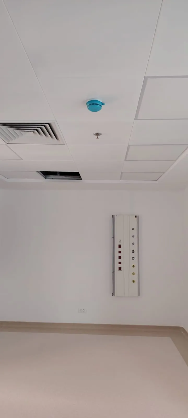Patient room with a bed head unit carrying medical gas outlets, plus ceiling diffuser, sprinkler and smoke detector